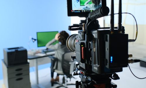 A camera filming a person in front of a screen.